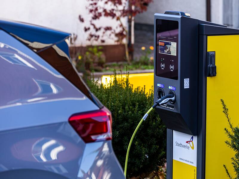 Eine grau-gelbe E-Ladestation für Elektroautos. Vor der Ladestation parkt ein graues Auto.