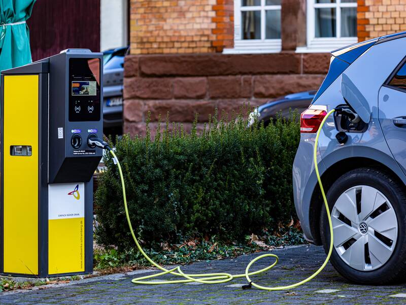 Eine gelb-graue E-Ladestation für Elektroautos. Von der Ladestation führt ein Ladekabel in die Tanköffnung eines grauen Autos.
