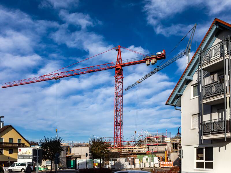 Eine Hausbaustelle mit einem roten Kran vor blauem, leicht bewölktem Himmel.