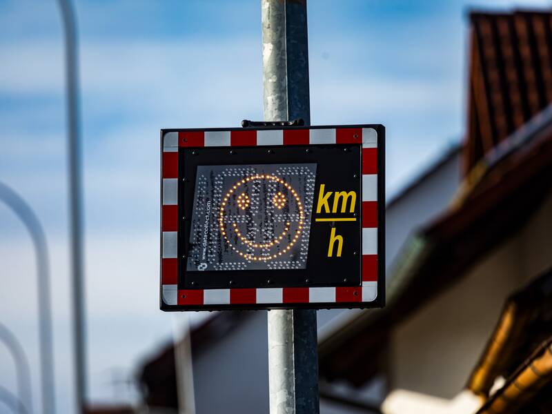 Eine Geschwindigkeitsanzeige, die ein lachendes Gesicht zeigt und an einem Laternenpfosten befestigt ist.